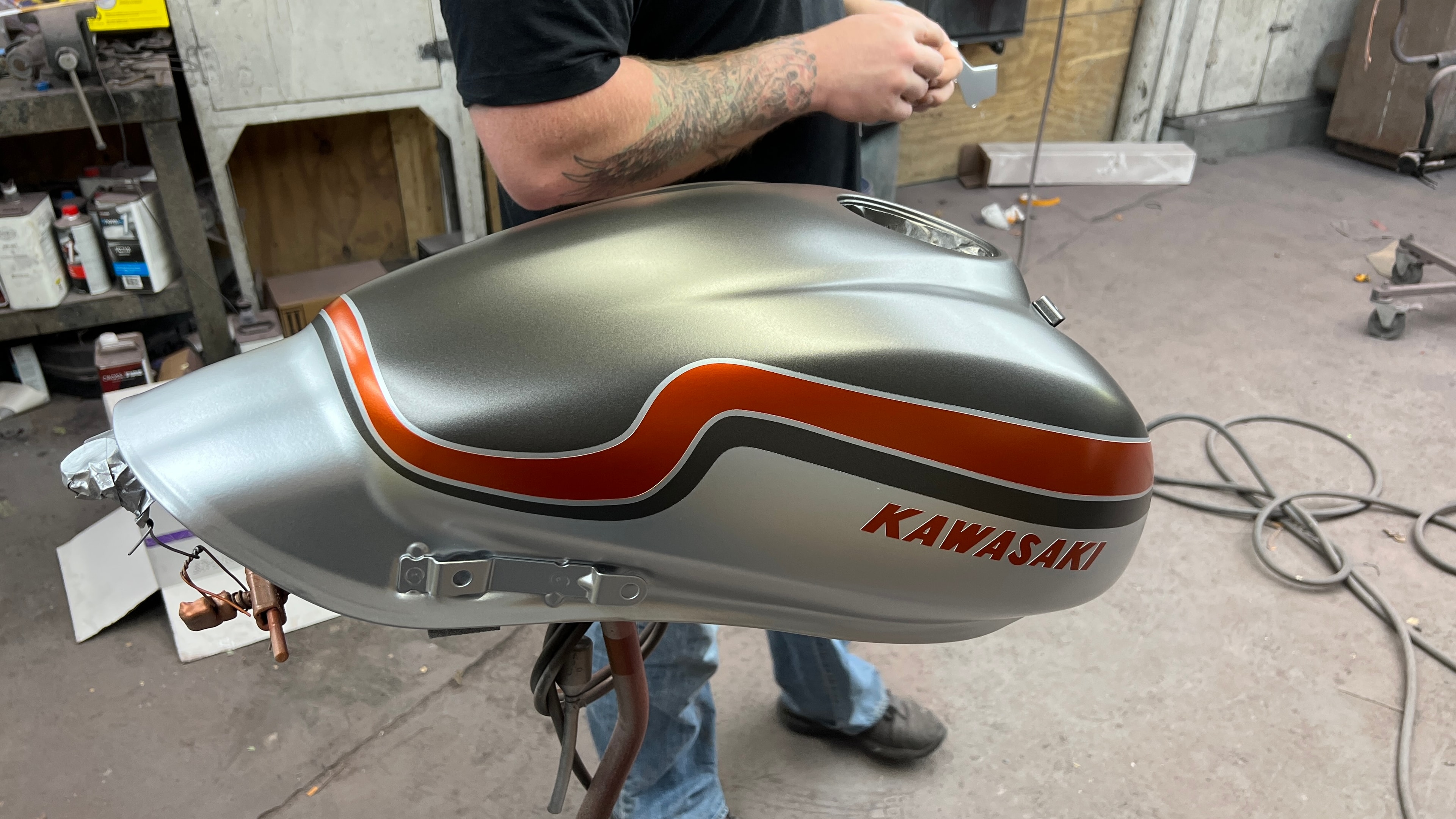 Kawasaki Vulcan S Cafe — tank off the bike in the shop, full wave stripe layout in Platinum Silver and Pearl Burnt Orange