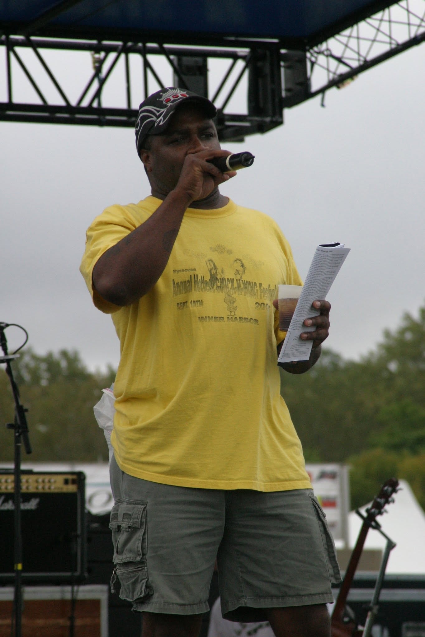 2006 Chick-N-Wing Festival — MC in Chick-N-Wing Festival shirt speaking at stage microphone