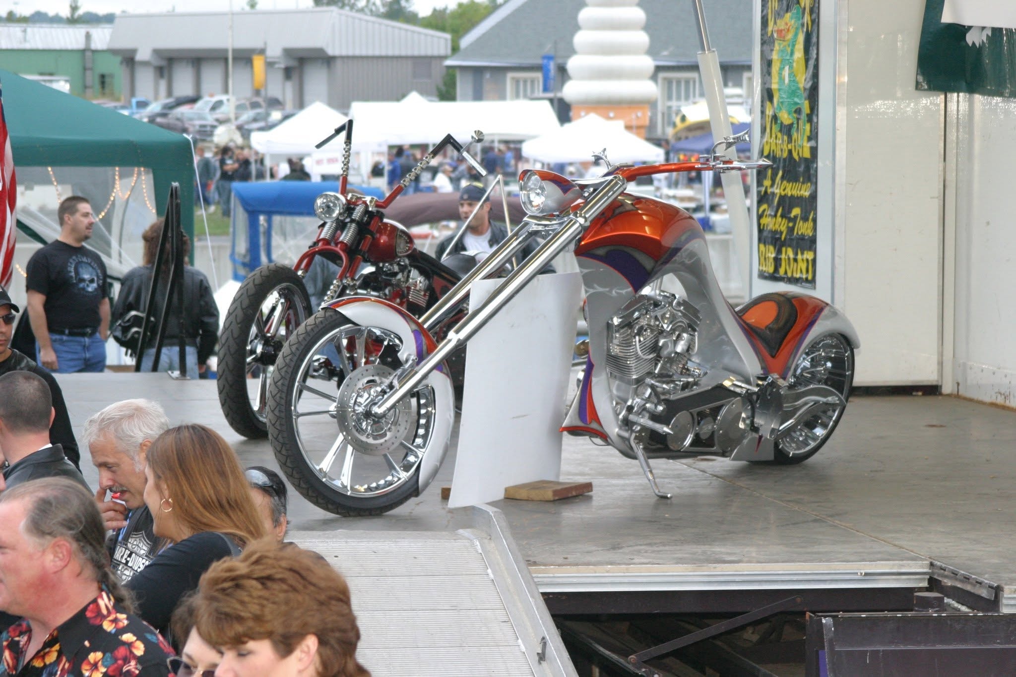 2006 Chick-N-Wing Festival — two custom choppers on stage with crowd and Dinosaur Bar-B-Que banner in background