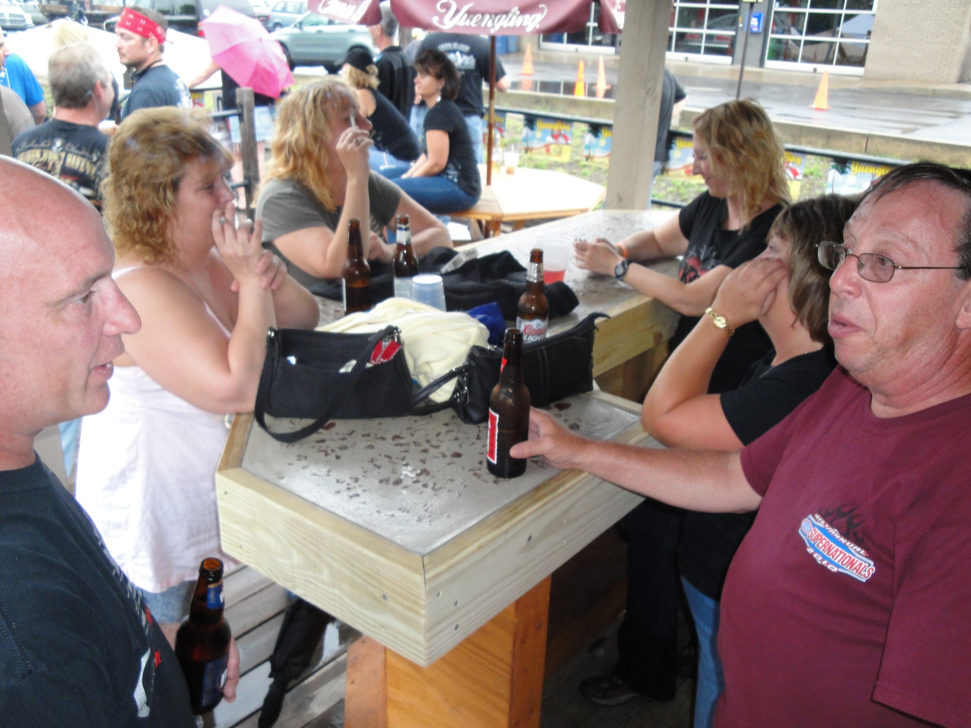 Higie's Iron Horse Saloon Summer BBQ Series — group at outdoor picnic tables under Yuengling umbrella in rain