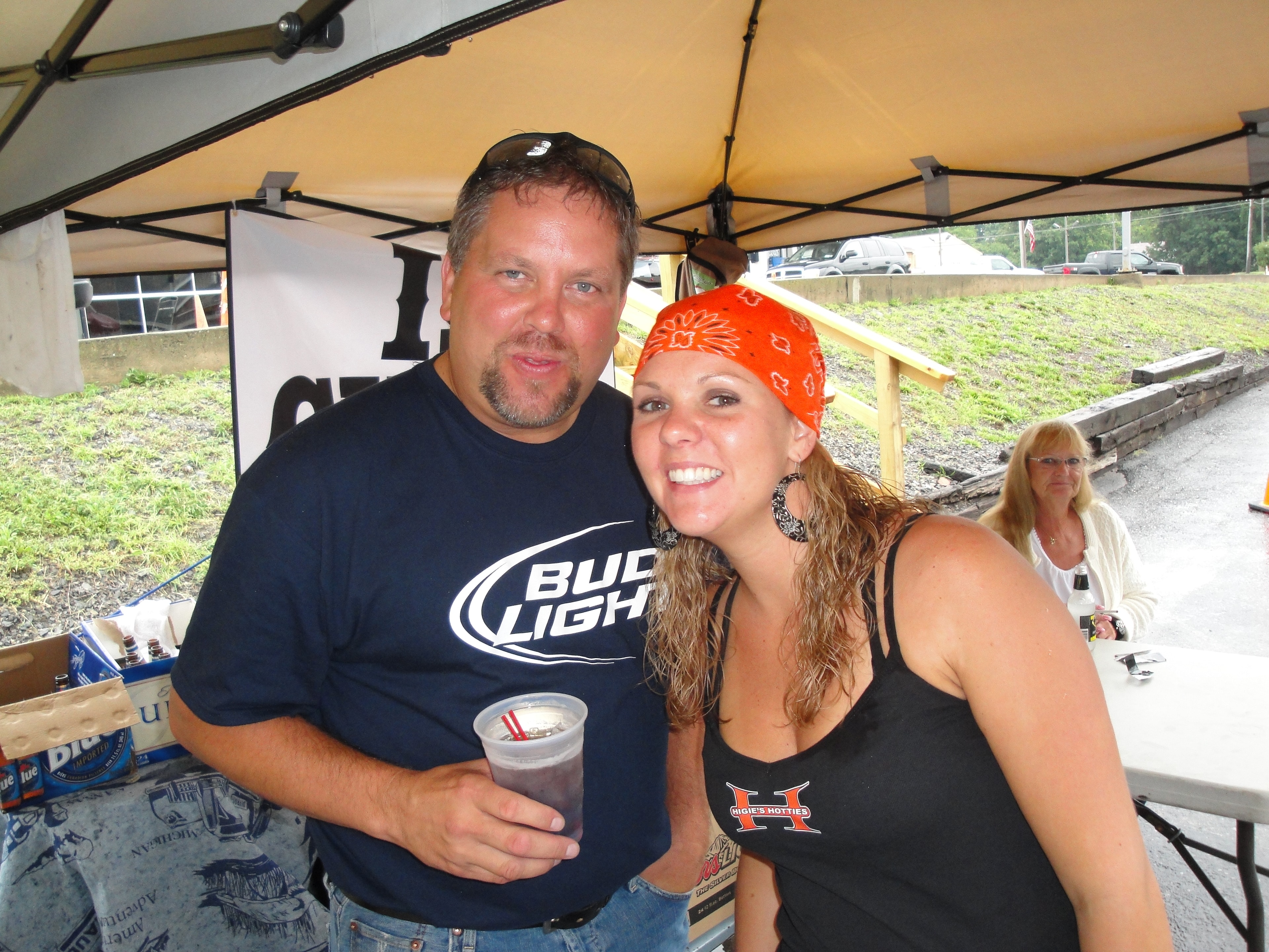 Higie's Iron Horse Saloon Summer BBQ Series — man in Bud Light shirt and woman in Higie's Hotties tank under event tent