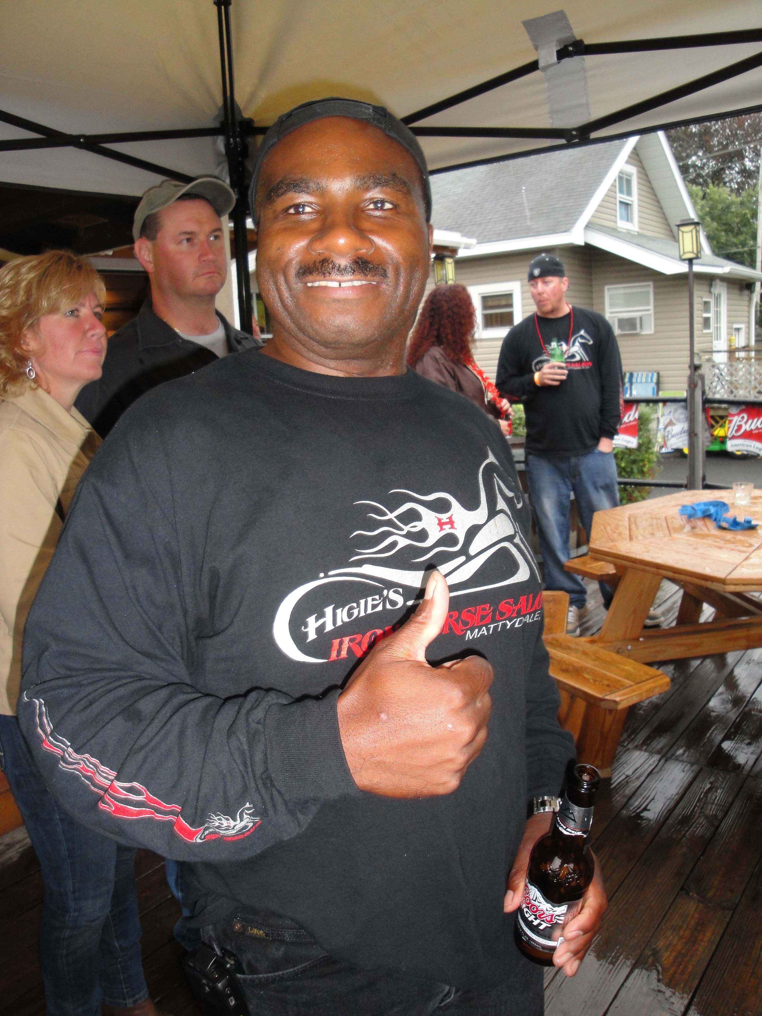 Higie's Iron Horse Saloon Summer BBQ Series — man in Higie's Iron Horse Saloon shirt pointing at logo with crowd behind