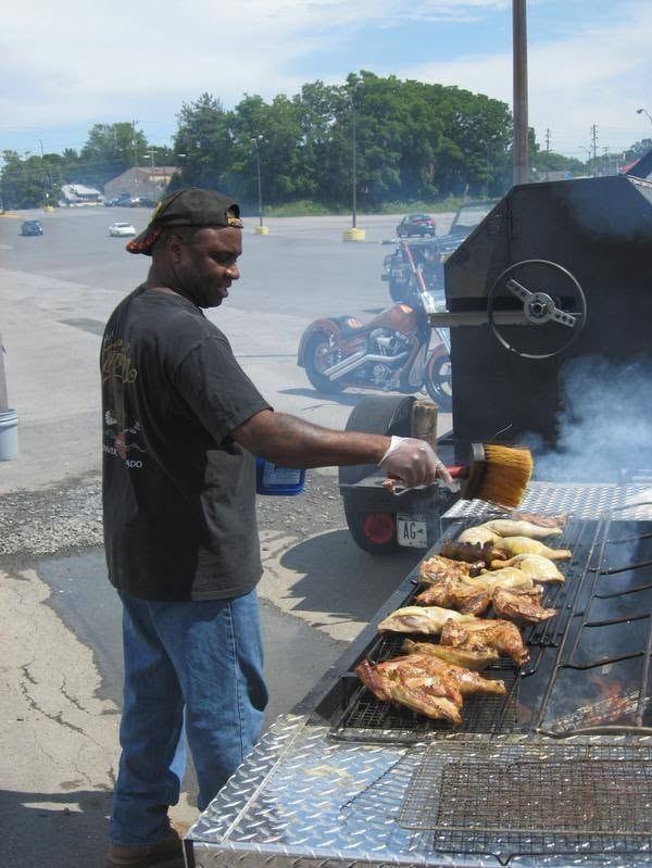 Woody's Pirate Party — man grilling chicken wings on large outdoor smoker with Harley in background