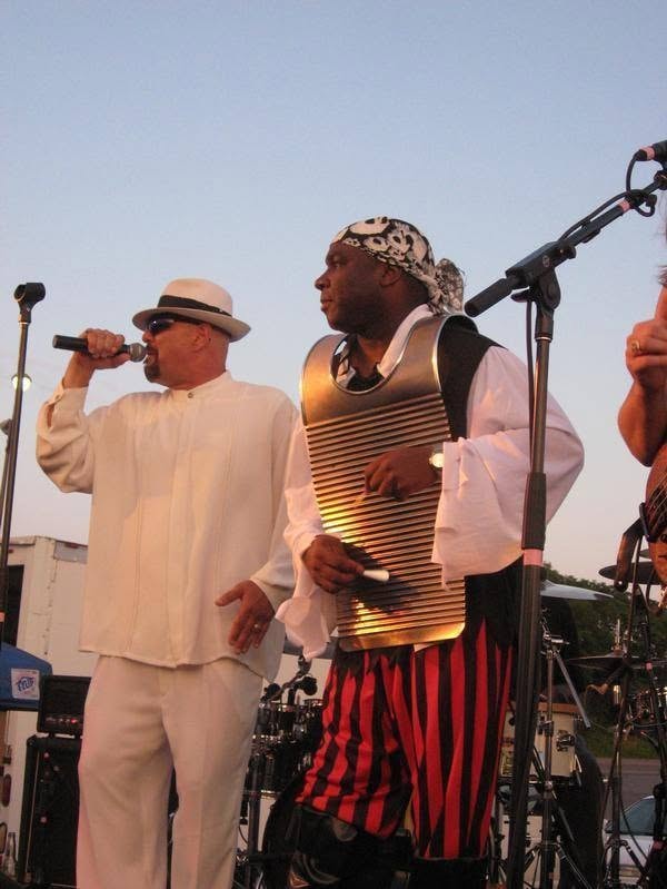 Woody's Pirate Party — singer in white suit and pirate washboard player performing on outdoor stage at dusk