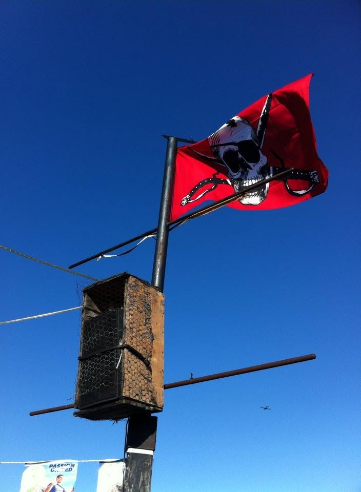 Woody's Pirate Party — red Jolly Roger skull and crossbones flag flying against blue sky outside the venue
