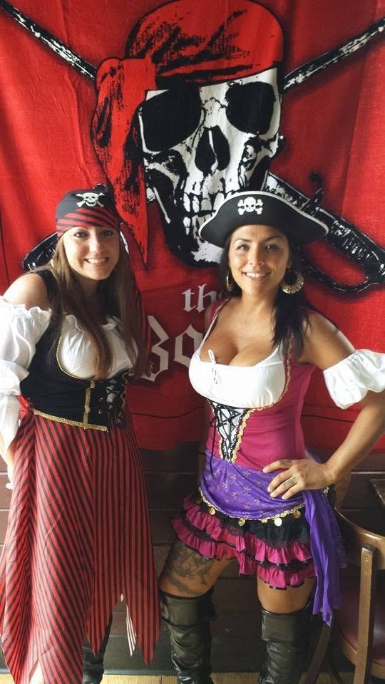 Woody's Pirate Party — two women in full pirate wench costumes posing in front of large skull and crossbones banner