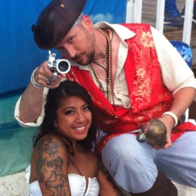 Woody's Pirate Party — large group of pirates and mermaids with man biting sword at tropical backdrop