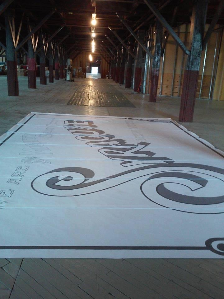 Design layout for the "We Are the Mighty Salt City" mural — full-scale artwork laid out on the warehouse floor