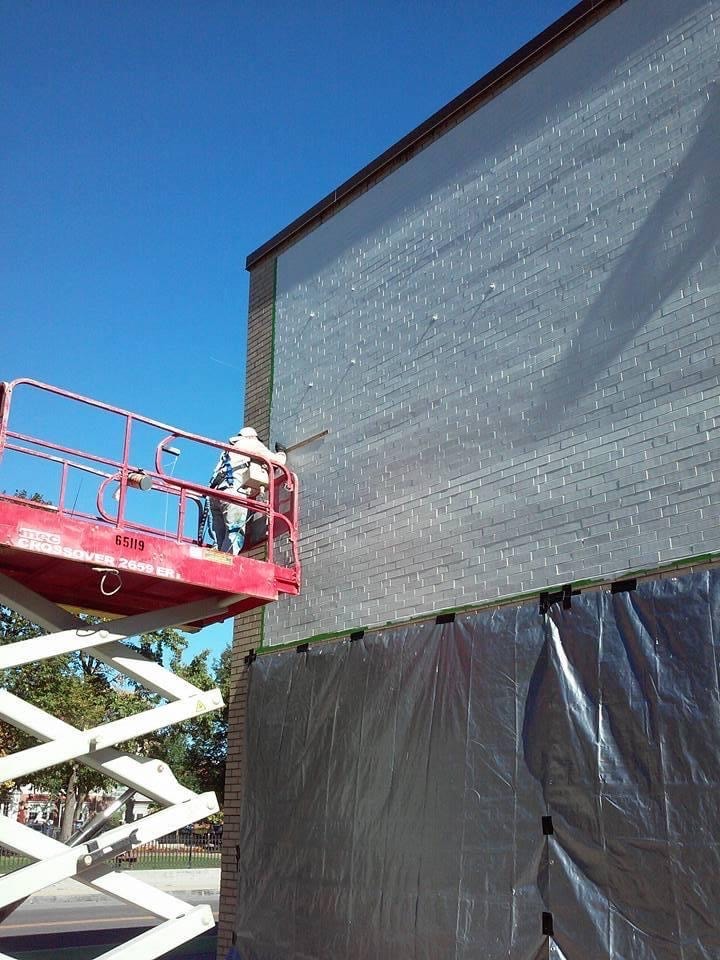 Base coat in progress — grey primer applied to the full mural field from a scissor lift
