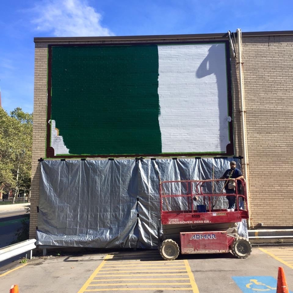 Green and white base coat blocked in — mural field half painted, Marcus on the scissor lift