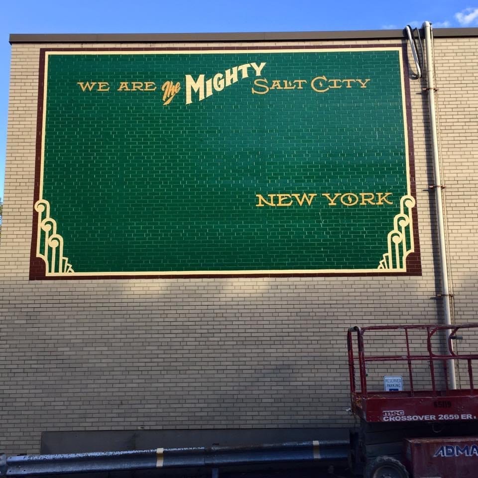 "We Are the Mighty Salt City — New York" text complete; "Syracuse" stencil being positioned