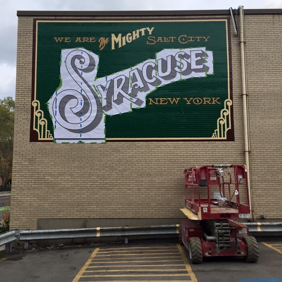 "Syracuse" lettering stencil fully applied and being painted in — mural nearing completion