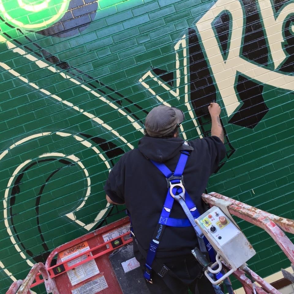 Close-up of Marcus on the scissor lift hand-painting the cream scroll lettering detail