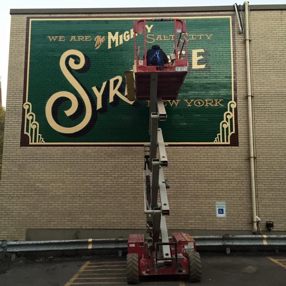 Mural near completion viewed from street level with scissor lift in foreground