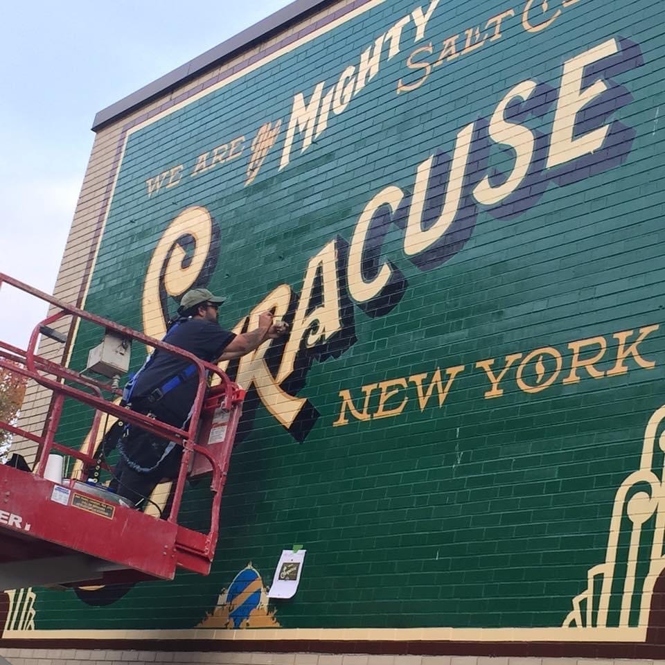 Marcus airbrushing the shadow detail on the large "Syracuse" lettering from the scissor lift basket