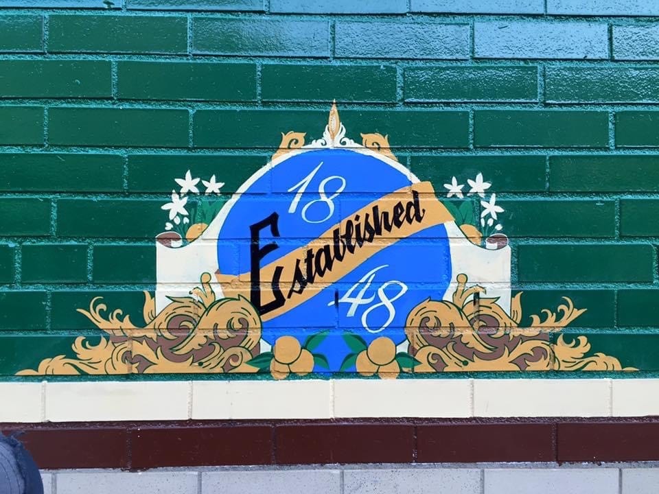 Detail of the "Established 1848" medallion — blue circle, gold scroll work, and white star flowers