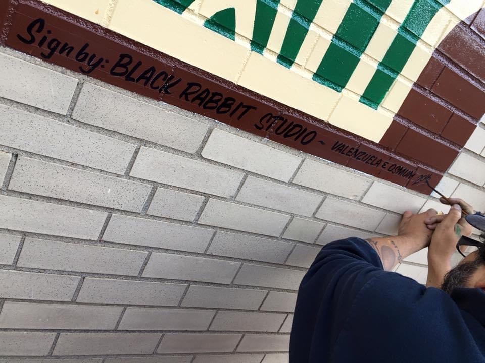 Marcus hand-lettering the "Sign by: Black Rabbit Studio — Valenzuela & Osmun" credit line