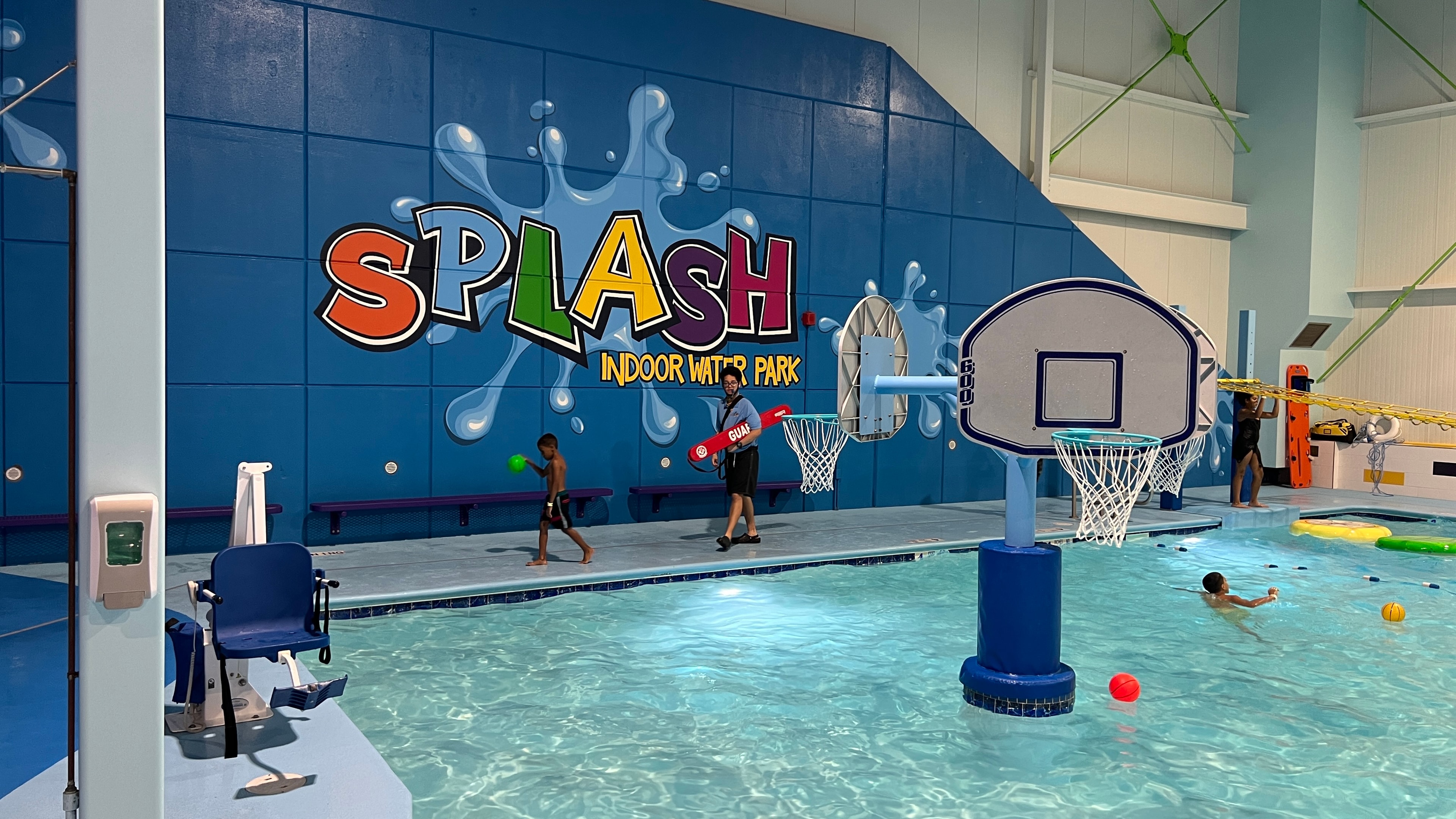 Splash Indoor Water Park facility in use — completed mural visible on the back wall with pool and basketball hoops in foreground