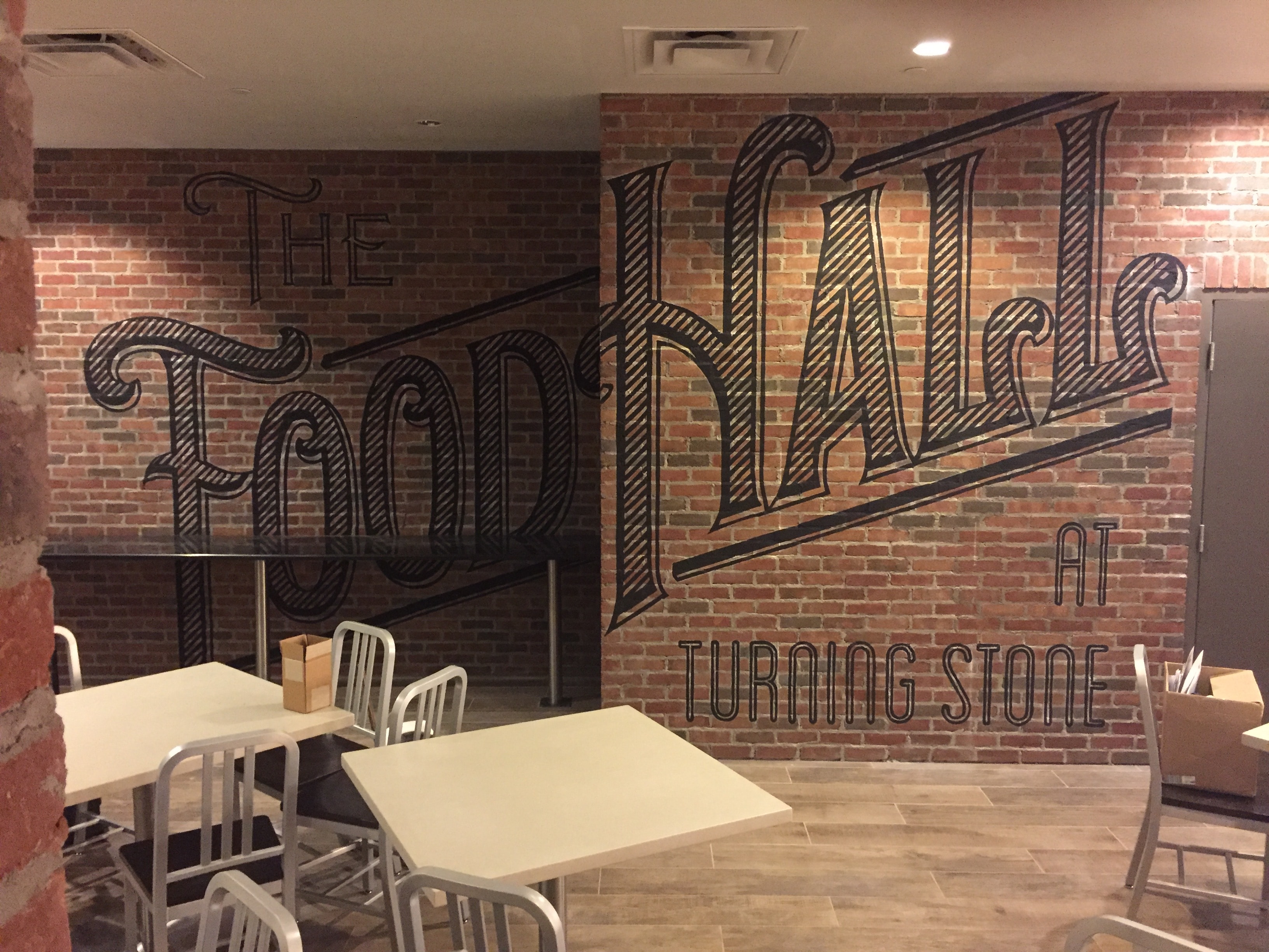 The Food Hall at Turning Stone — hand-painted gothic lettering mural on exposed brick wall, close-up view